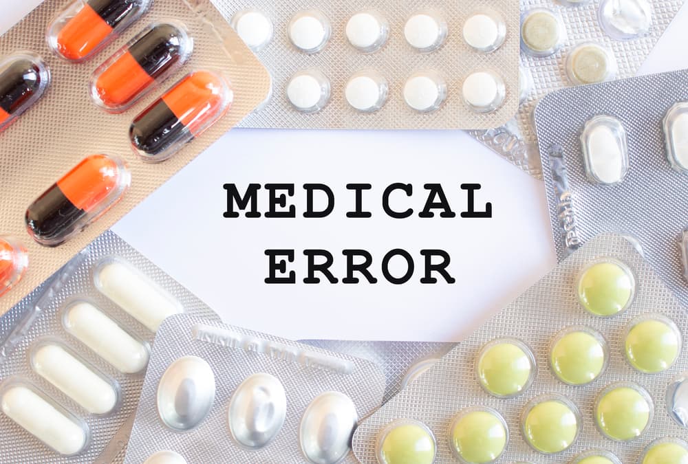 Text MEDICAL ERROR on a white background. There are different medicines around.