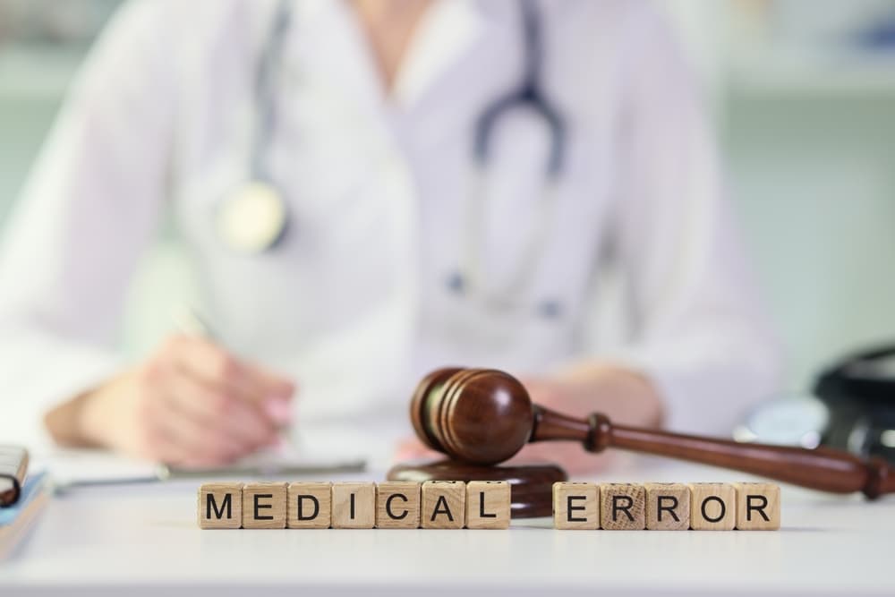 Words medical errors collected from wooden cubes with judge's gavel on table, doctor with stethoscope in background.
