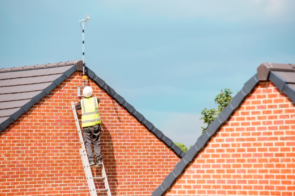 Construction worker standing on a ladder while working on a roof, showing a common fall hazard on NYC job sites.