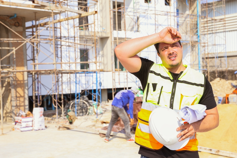 Worker wiping sweat on a construction site in extreme heat, illustrating weather-related safety risks.