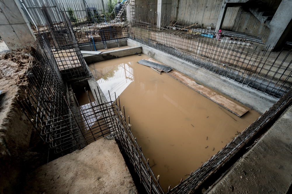 Flooded construction site with standing water after heavy rain, creating slip and collapse hazards.