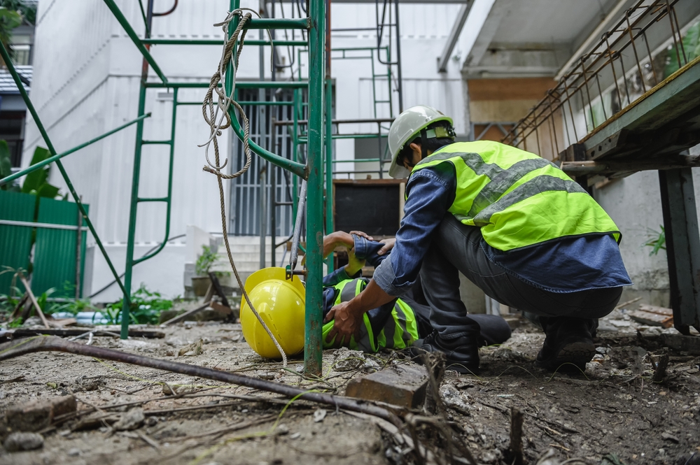 Worker assisting an injured coworker after a fall on a New York City construction site.