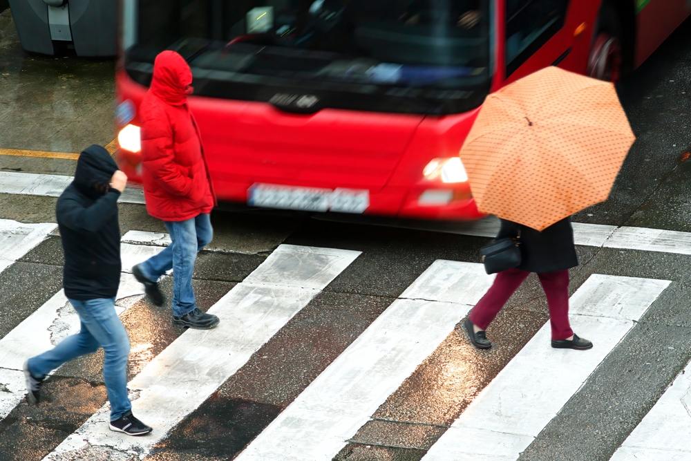 Pedestrians crossing a wet crosswalk in rainy weather as a city bus drives past
