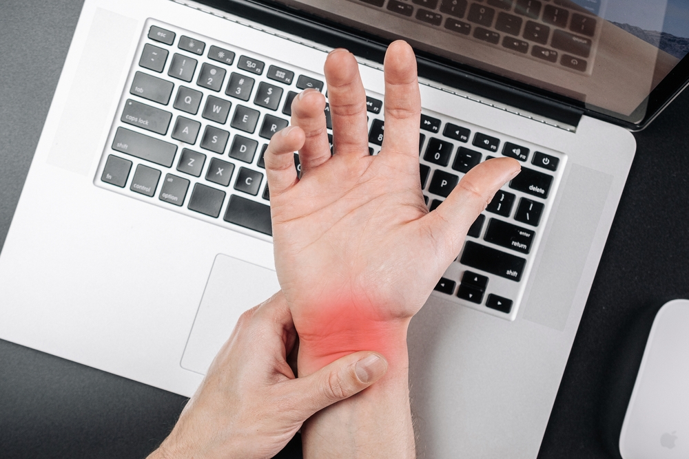 Worker holding painful wrist while using a laptop, indicating a possible work-related injury that may require OSHA recording