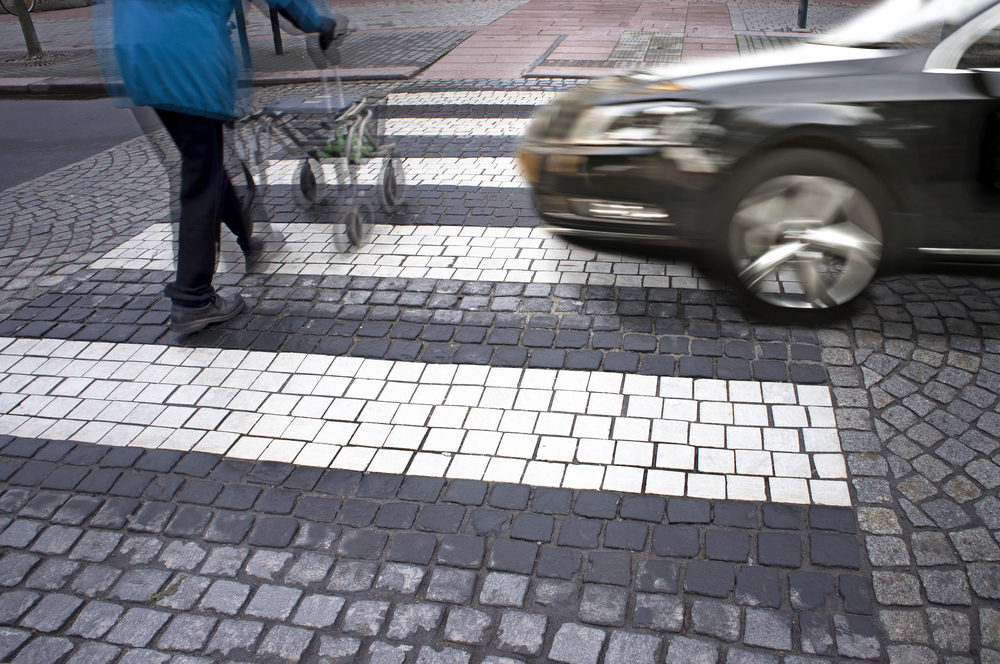 Car speeding through a crosswalk as a pedestrian with a walker crosses, illustrating a common cause of pedestrian accidents.